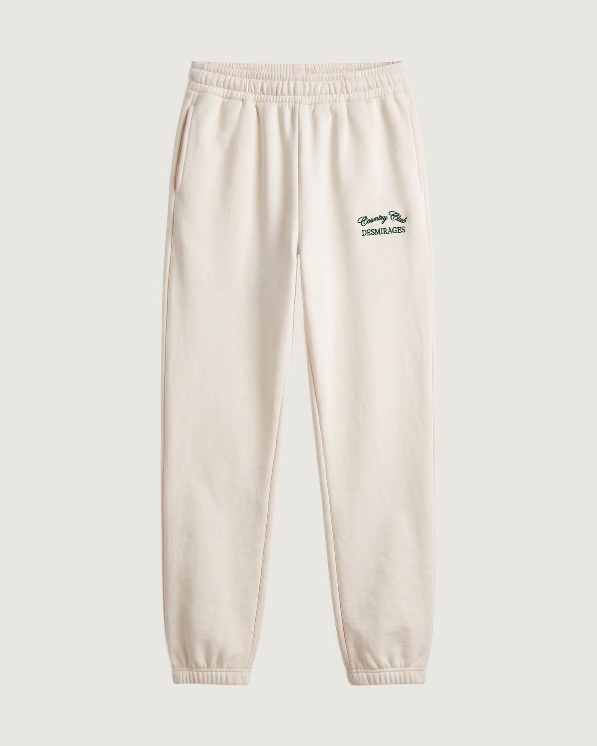 Cream DESMIRAGES Country Club sweatpants with an elastic waistband, cuffed ankles and green embroidered logo, front view.
