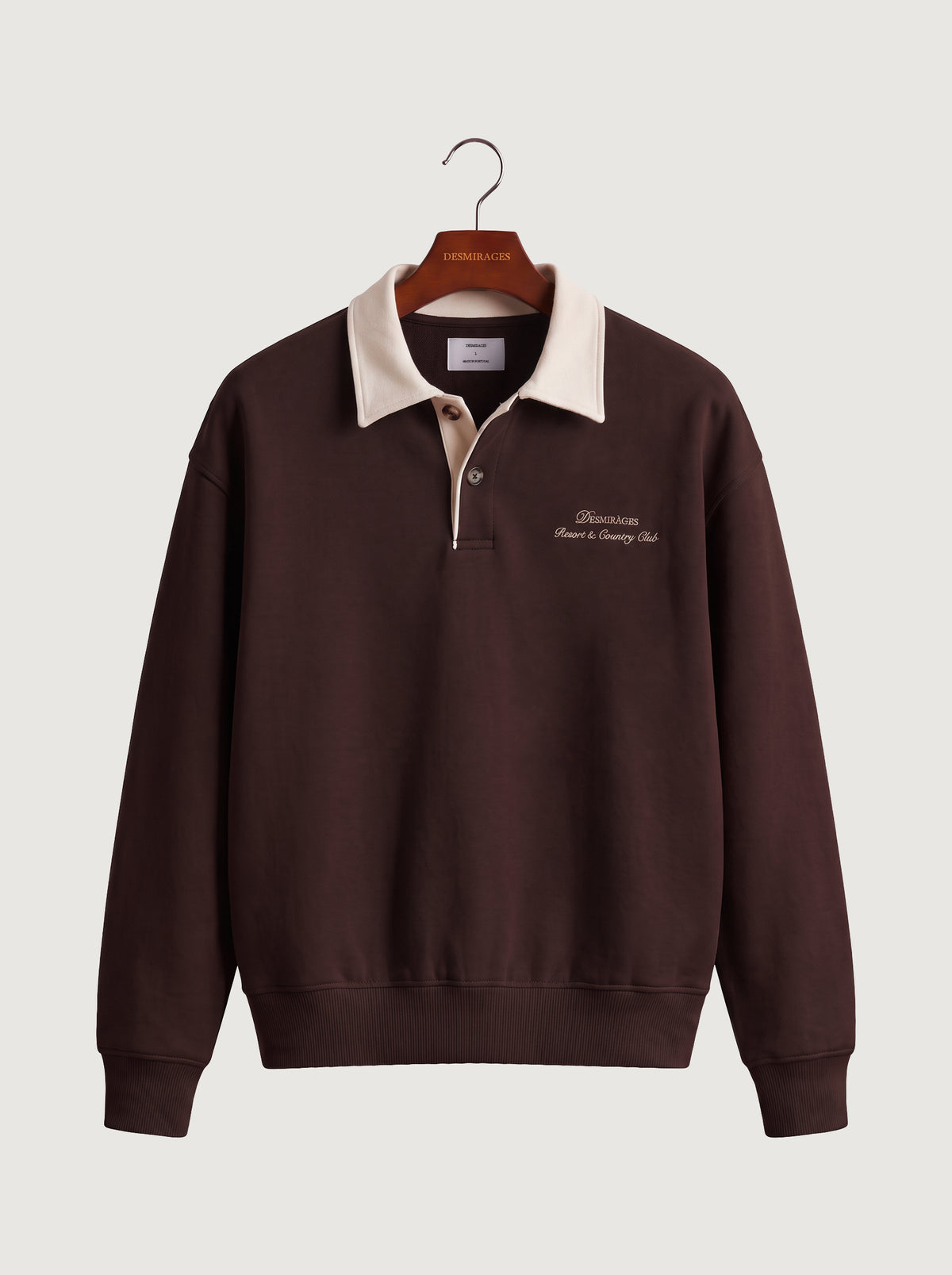 Chocolate brown polo sweatshirt with cream collar and embroidered DESMIRAGES logo, front view on a hanger.
