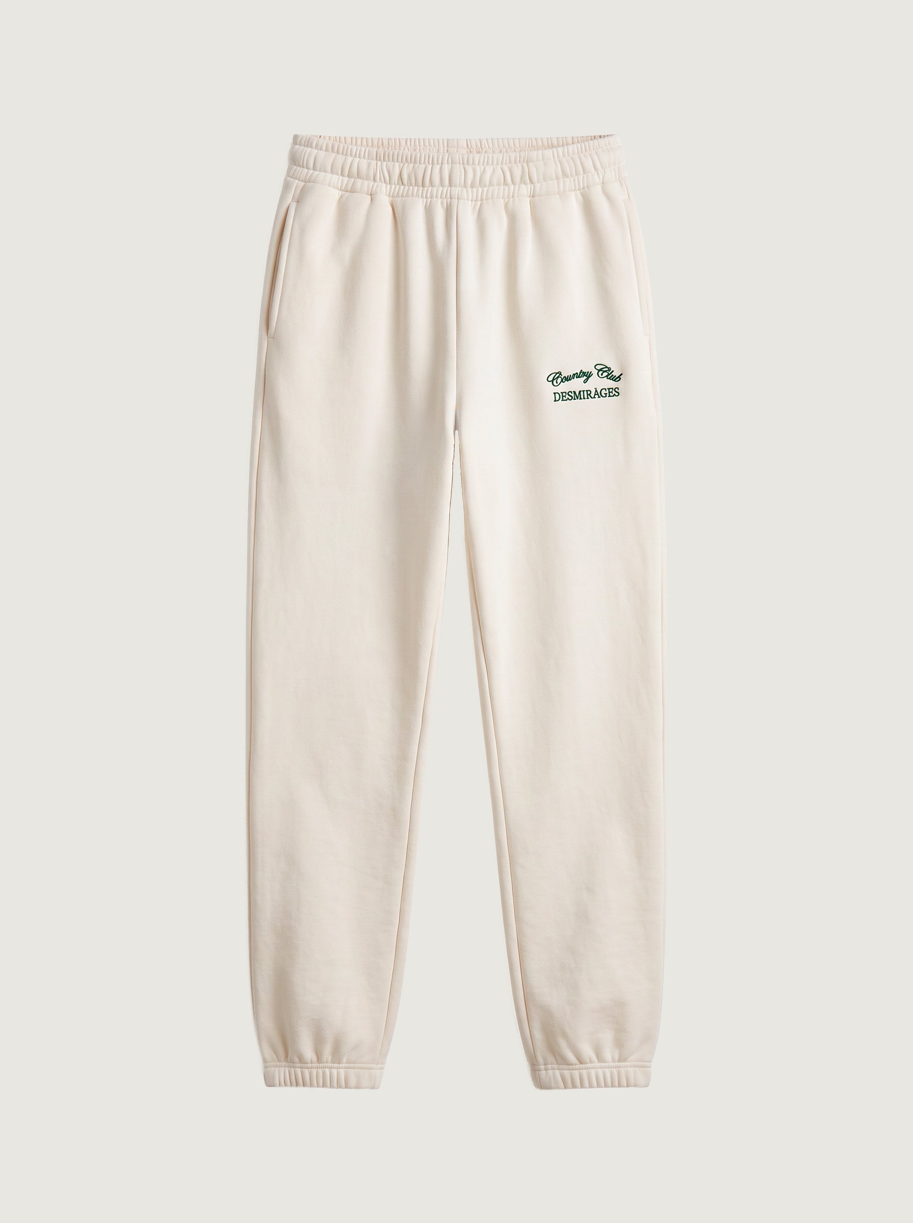 Cream DESMIRAGES Country Club sweatpants with an elastic waistband, cuffed ankles and green embroidered logo, front view.